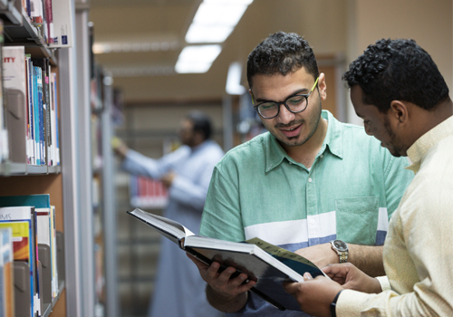 Two students in a library looking through a Master of Business Administration textbook