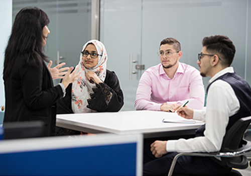 A male and two females completing their MBA in UAE are looking at a screen together