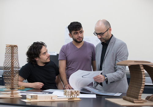 Two students looking at a book with their bachelor of architecture lecturer