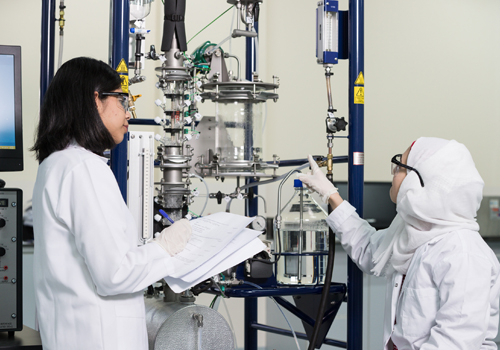 A Bachelor of Science in Chemical Engineering student is taking notes while a colleague points to lab equipment