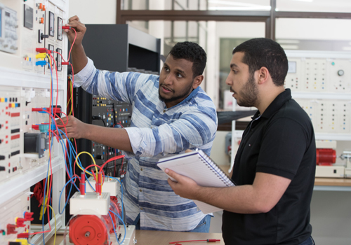 Two students following a Bachelor of Science in Electrical Engineering notebook to hook up an electrical panel