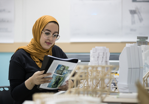 Female student sitting at a table going through a Bachelor of Interior Design Degree textbook