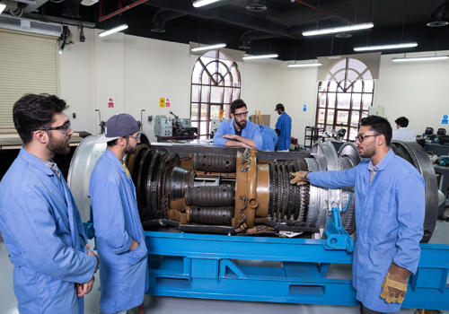 Mechanical Engineering lecturer showing students a piece of machinery in a workshop