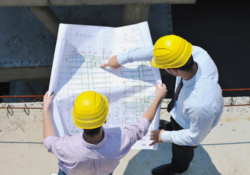 Two Master of Engineering Management graduates looking at engineering plans on site