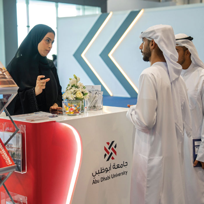 Group of professionals in formal attire collaborating around a laptop in a bright modern office.