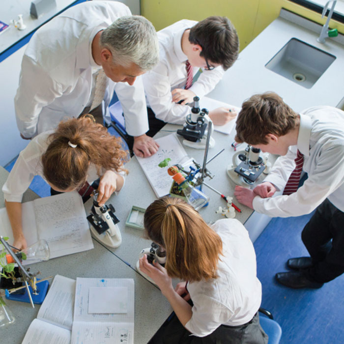 Group of professionals in formal attire collaborating around a laptop in a bright modern office.